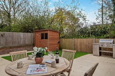 a wooden table with a bottle of wine and flowers on a patio at 3 Bed in Framlingham oc-f30353 in Framlingham