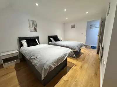 two beds in a room with white walls and wooden floors at A luxurious coach house in Colchester
