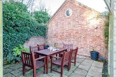 a wooden table with four chairs and a brick wall at Compass Barn, Wenhaston in Wenhaston