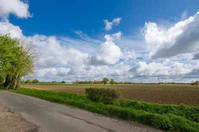 a dirt road next to a field with a cloudy sky at East Wing at Champaignes Toft, Mendlesham in Stowmarket