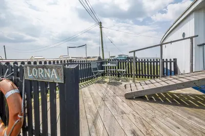 a wooden boardwalk with a bench next to a building at Lorna, Houseboat , West Mersea in West Mersea