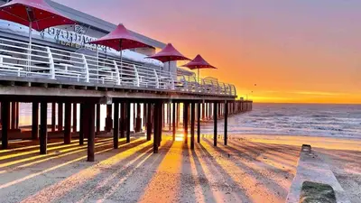 a pier with umbrellas on the beach at sunset at Modern 2 Bedroom Apartment with Sea view in Felixstowe