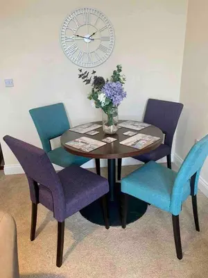 a dining room table with four chairs and a clock at Modern 2 Bedroom Apartment with Sea view in Felixstowe