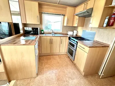 a kitchen with wooden cabinets and a stove top oven at Seashell Hideaway Caravan at Seawick Holiday Park in Clacton-on-Sea