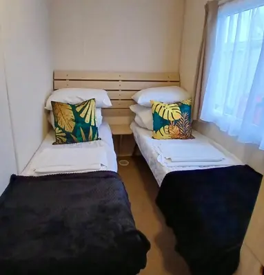 two beds in a small room with a window at Seashell Hideaway Caravan at Seawick Holiday Park in Clacton-on-Sea