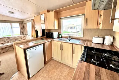 a kitchen with wooden cabinets and a sink and a stove at Seashell Hideaway Caravan at Seawick Holiday Park in Clacton-on-Sea