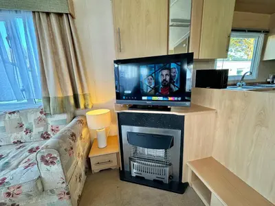 a living room with a flat screen tv on a fireplace at Seashell Hideaway Caravan at Seawick Holiday Park in Clacton-on-Sea
