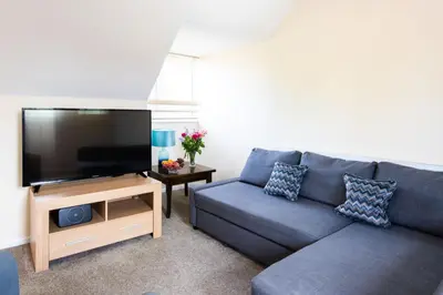 a living room with a blue couch and a flat screen tv at Dolphin Apartment, Thorpeness - Only a short stroll from the Beach, Thorpeness Lake, Country Club and Golf Club in Thorpeness