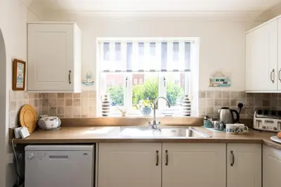 a kitchen with white cabinets and a sink and a window at 2 Admirals Walk by Aldeburgh Coastal Cottages in Thorpeness