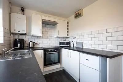 a kitchen with white cabinets and a black counter top at Hampstead Avenue in Great Clacton