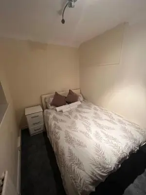 a small bedroom with a white bed and a night stand at Barnfield Rooms in Chelmsford