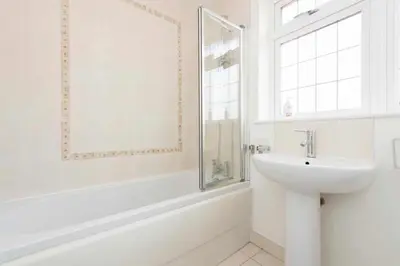 a white bathroom with a sink and a window at 5 Bed House in Romford 9 Beds in Havering atte Bower