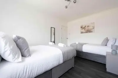 two beds in a bedroom with white walls and wood floors at 5 Bed House in Romford 9 Beds in Havering atte Bower