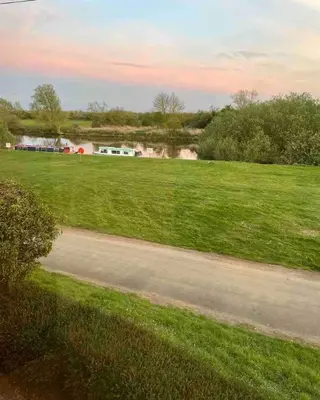a grassy field with a road and a river at Outbuilding with river views in Cambridgeshire in Holywell