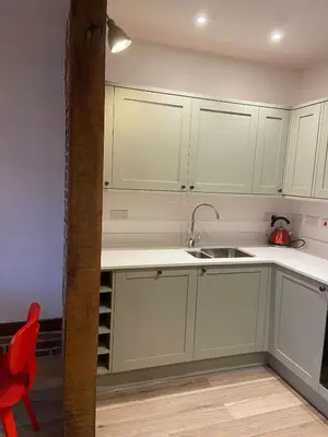 a kitchen with white cabinets and a sink and a red chair at Charming 2-Bedroom Cottage in Cambridgeshire in West Wratting