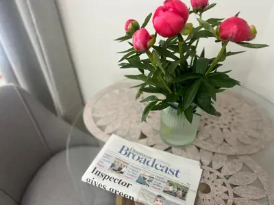 a table with a newspaper and a vase with pink flowers at 2 Bedroom Apartment 11 Minutes From Stansted Airport in Great Dunmow