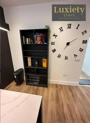 a large clock on a wall next to a book shelf at Sleek & Stunning 2BR APT By Luxiety Stays Short Lets & Serviced Accommodation Southend on sea With Free WiFi, Smart TV, Netflix in Southend-on-Sea
