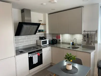 a kitchen with white cabinets and a microwave and a table at Central Leigh, on the Broadway, private gated parking, balcony in Southend-on-Sea