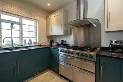 a kitchen with green cabinets and a stove top oven at 3 The Coastguards, Thorpeness - Only a stones throw from the Beach and very close to famous boating Meare, Country Club and Golf Club - Aldeburgh Coastal Cottages in Thorpeness