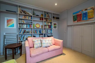 a living room with a pink couch and book shelves at 3 The Coastguards, Thorpeness - Only a stones throw from the Beach and very close to famous boating Meare, Country Club and Golf Club - Aldeburgh Coastal Cottages in Thorpeness