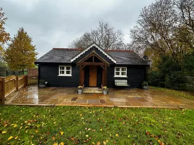 a small black house with a patio in a yard at The Gate Lodge - Pet Free - Near Finchingfield & Saffron Walden in Great Sampford
