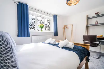 a bedroom with a bed with blue curtains and a window at 2 Bed Elegant home with Parking in Harlow in Harlow