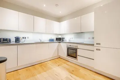 a kitchen with white cabinets and a wooden floor at Lovely Central Brentwood Flat in Brentwood