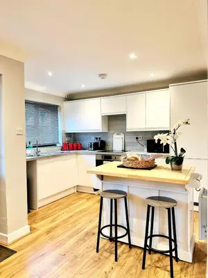 a kitchen with white cabinets and a island with two bar stools at Modern House Soham Town Centre in Soham