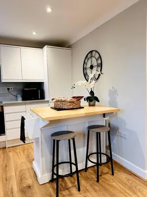 a kitchen with a counter with stools and a clock on the wall at Modern House Soham Town Centre in Soham