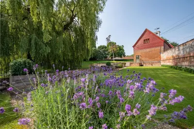 a garden with purple flowers and a red barn at Belchamp Hall Hayloft in Belchamp Otten