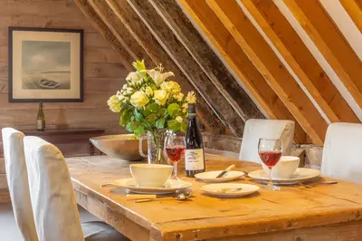 a wooden table with wine glasses and a vase of flowers at Belchamp Hall Hayloft in Belchamp Otten