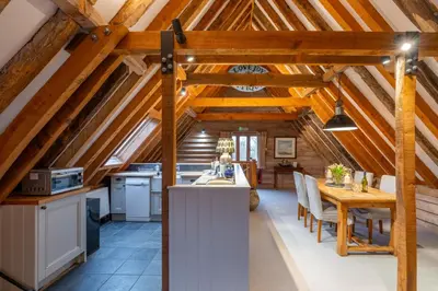 a kitchen and dining room in a barn conversion with wooden beams at Belchamp Hall Hayloft and Stables in Belchamp Otten