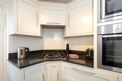 a kitchen with white cabinets and a stove top oven at Emeny Cottage - Aldeburgh Coastal Cottages in Aldeburgh