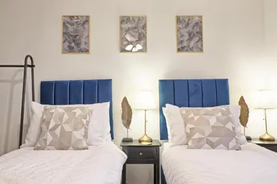 two beds with blue headboards in a bedroom at Stylish 5-Bed London Residence Featuring Garden, Parking & High-Speed Internet in Nevendon