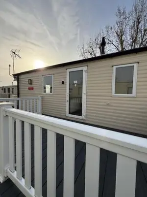 a house on a deck with a white railing at 6 Beds 2 Sofa bed Family friendly - unlimited Wi-Fi, Warm, Cozy Sun decking Caravan at Seawick Holiday Park in Saint Osyth
