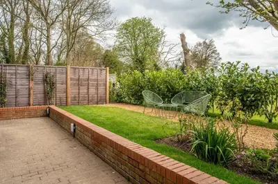 a garden with a brick wall and two chairs in the grass at Luxury self contained one bedroom - Sawbridgeworth in Sheering