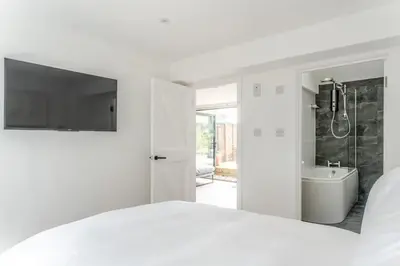 a white bedroom with a shower and a bath tub at Modern self contained one bedroom with garden in Sheering