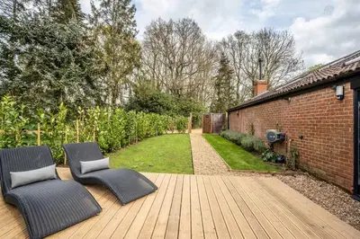 a wooden deck with two chairs and a brick wall at Modern self contained one bedroom with garden in Sheering