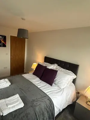 a bedroom with a bed with white sheets and purple pillows at Mango Cottage in Thorndon