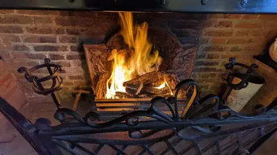 a brick fireplace with a fire in it at Grade 1 Listed Farm House 14 ppl 45 mins London in Fyfield