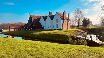 a large house on a hill with a river in front at Grade 1 Listed Farm House 14 ppl 45 mins London in Fyfield