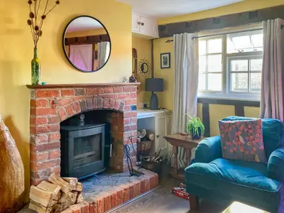 a living room with a brick fireplace and a mirror at Sunny Meadow Cottage in Sudbury