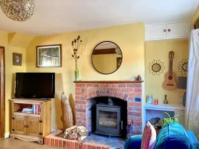 a living room with a brick fireplace and a mirror at Sunny Meadow Cottage in Sudbury