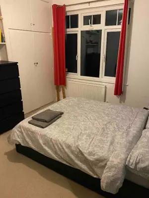a bedroom with a bed and a window with red curtains at Cosy room in Faulkbourne