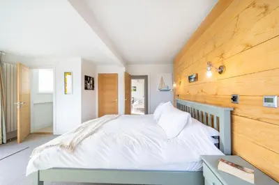 a bedroom with a large white bed with a wooden wall at Chicoutimi in Thorpeness