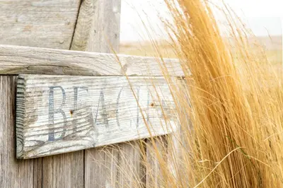 a wooden sign on a wooden fence with tall grass at Chicoutimi in Thorpeness