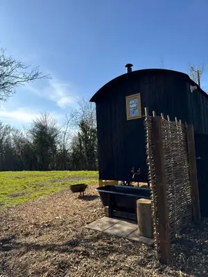 a black building with a bath tub in a field at 'Russet' Hut on fruit farm in Charsfield