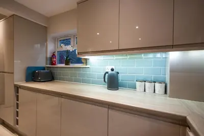 a kitchen with white cabinets and blue tiles at High Street 200A in Wickham Market