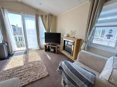 a living room with a couch and a tv and windows at Lovely 6 Berth Caravan With Decking At Suffolk Sands Holiday Park Ref 45005Hc in Felixstowe