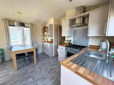 a kitchen with white cabinets and a sink and a table at Lovely 6 Berth Caravan With Decking At Suffolk Sands Holiday Park Ref 45005Hc in Felixstowe